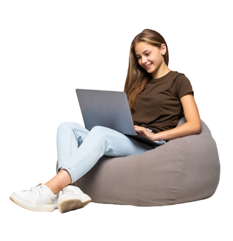 A youbng girl sitting on a bean bag on the floor smiling looking at her laptop and working